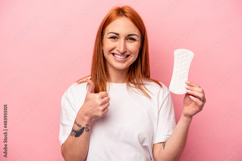 Young caucasian woman holding sanitary napkin isolated on pink background smiling and raising thumb up Young caucasian woman holding sanitary napkin isolated on pink background smiling and raising thumb up