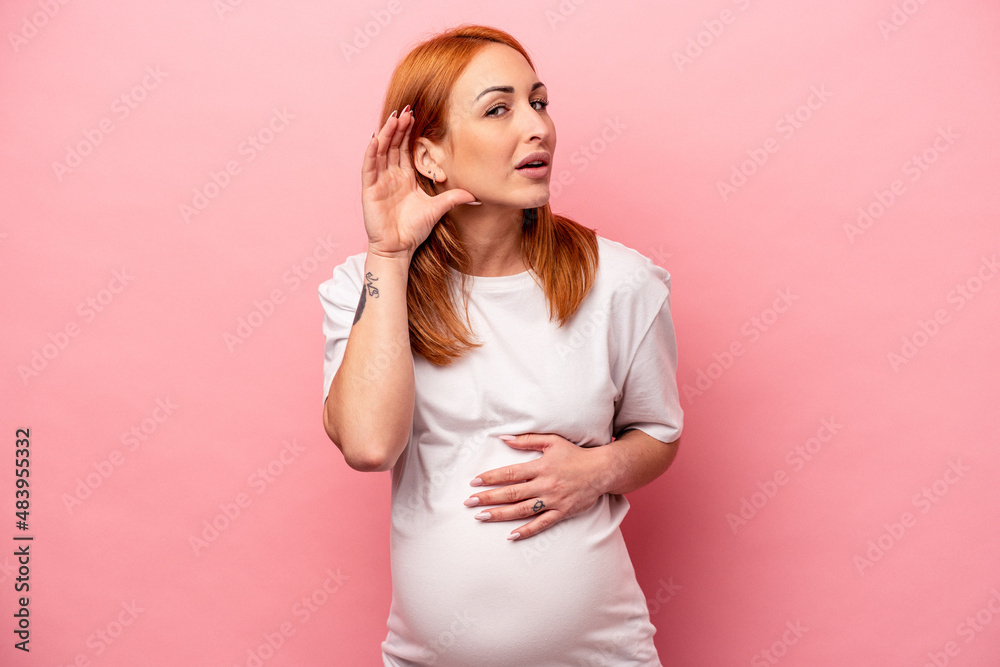 Young caucasian pregnant woman isolated on pink background trying to listening a gossip. Young caucasian pregnant woman isolated on pink background trying to listening a gossip.