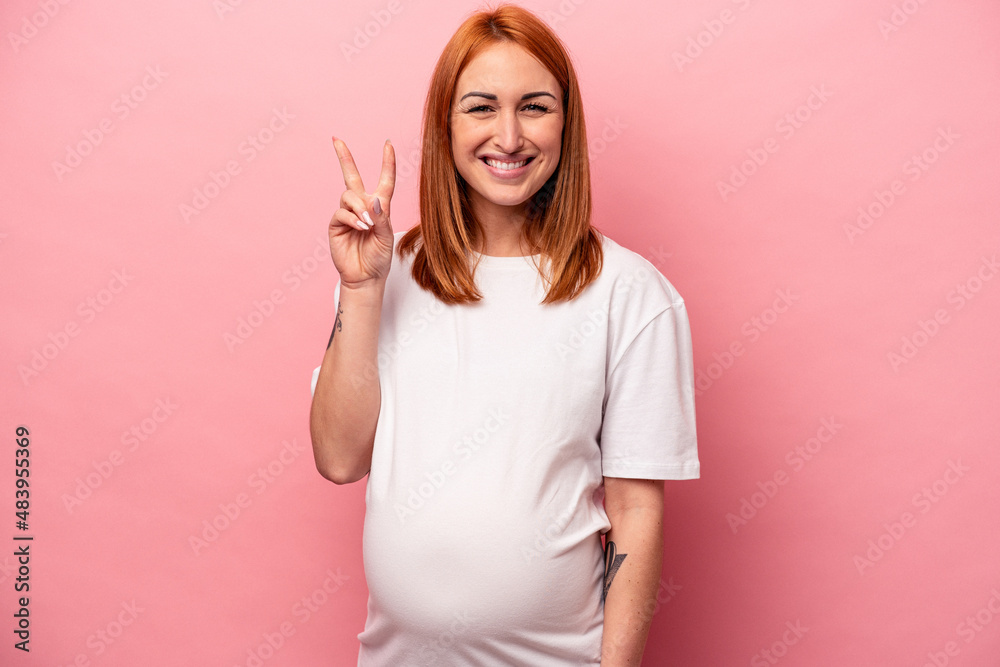 Young caucasian pregnant woman isolated on pink background showing number two with fingers.
