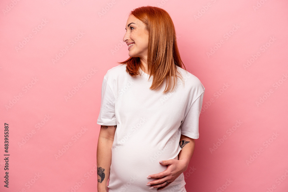 Young caucasian pregnant woman isolated on pink background looks aside smiling, cheerful and pleasant. Young caucasian pregnant woman isolated on pink background looks aside smiling, cheerful and pleasant.