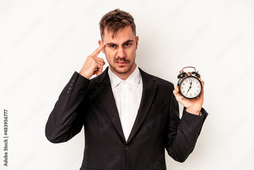 Young caucasian business man holding alarm clock isolated on white background showing a disappointment gesture with forefinger. Young caucasian business man holding alarm clock isolated on white background showing a disappointment gesture with forefinger.