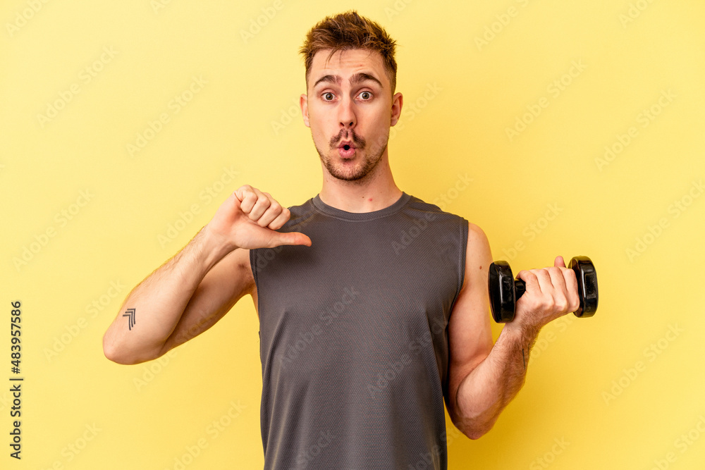 Young sport man holding a dumbbell isolated on yellow background feels proud and self confident, example to follow.