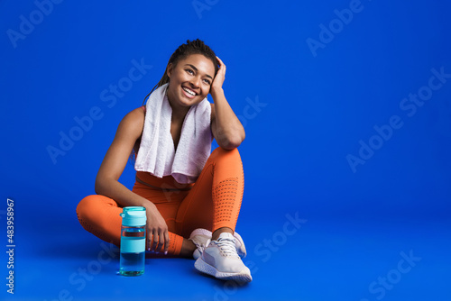 Black young sportswoman smiling while sitting on floor