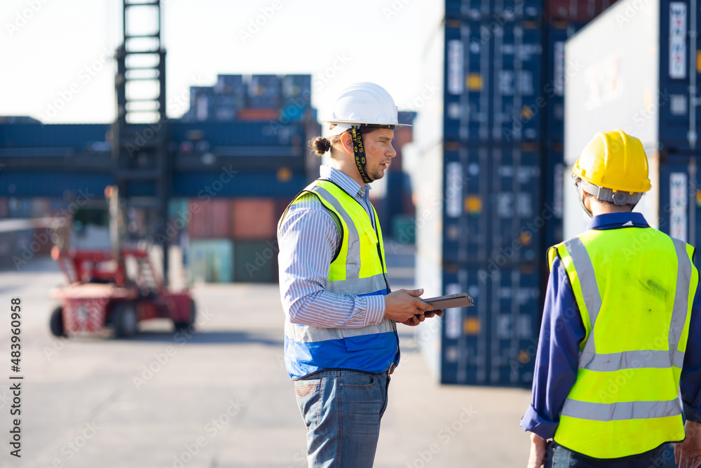 Two caucasian man engineer worker wearing hardhat safety helmet and vest working in logistic shipping yard. Marine and carrier insurance concept. Cargo container yard. Two caucasian man engineer worker wearing hardhat safety helmet and vest working in logistic shipping yard. Marine and carrier insurance concept. Cargo container yard.