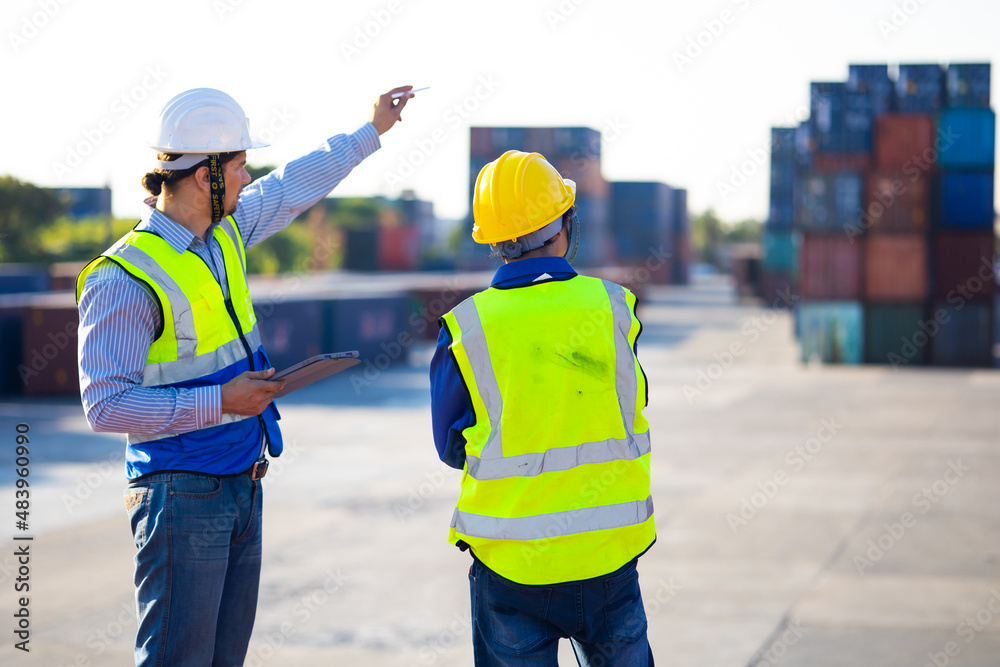 Two caucasian man engineer worker wearing hardhat safety helmet and vest working in logistic shipping yard. Marine and carrier insurance concept. Cargo container yard. Two caucasian man engineer worker wearing hardhat safety helmet and vest working in logistic shipping yard. Marine and carrier insurance concept. Cargo container yard.