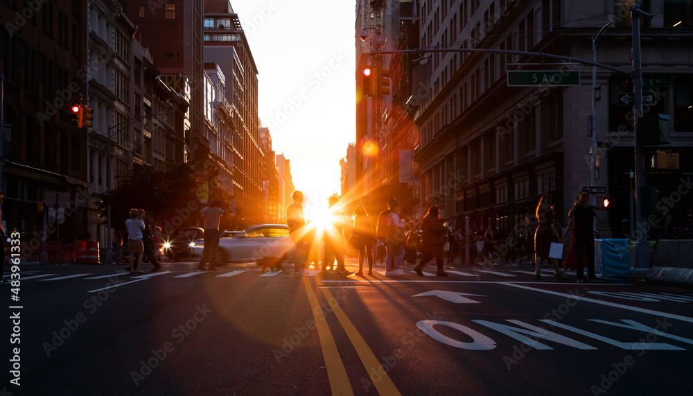 Busy street scene with people and cars at a crowded intersection on 5th Avenue in Manhattan New York City with sunset in the background