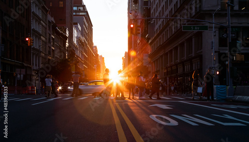 Busy street scene with people and cars at a crowded intersection on 5th Avenue in Manhattan New York City with sunset in the background © deberarr