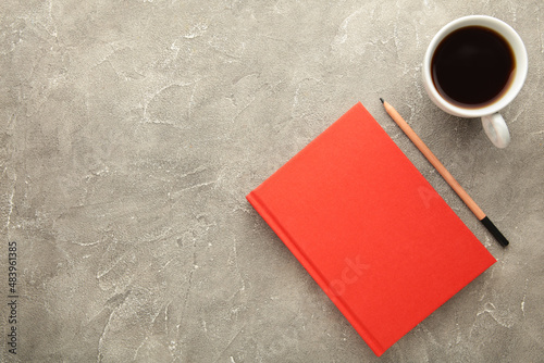 Red notebook with coffee cup and pencil on grey background. Flat lay, creative workspace office. Business-education concept with copy space.