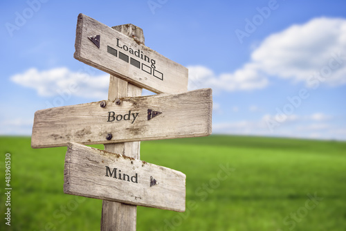 Loading text and bar with body mind quote engraved on wooden signpost outdoors on green field with blue sky.