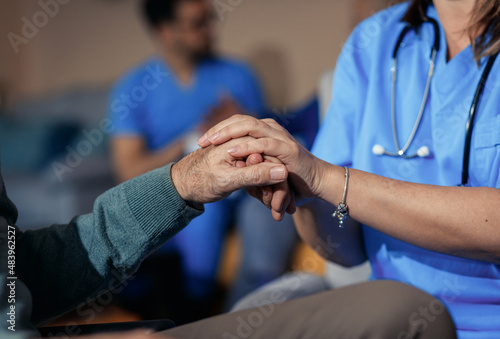 Close up of female nurse holding hand to senior man at nursing home.