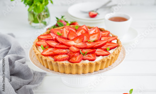 Strawberry tart with custard cream on a plate on a white wooden background. Copy space.