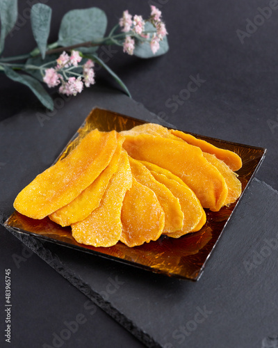 A few pieces of dried mango on a square glass plate on a black background. Healthy desserts, vegetarianism, healthy food concept