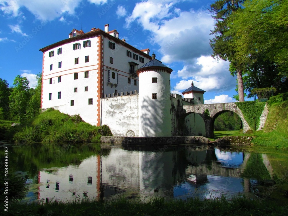 Beautiful medieval Sneznik castle in Notranjska, Slovenia with a reflection in the water and white clouds in blue sky behind