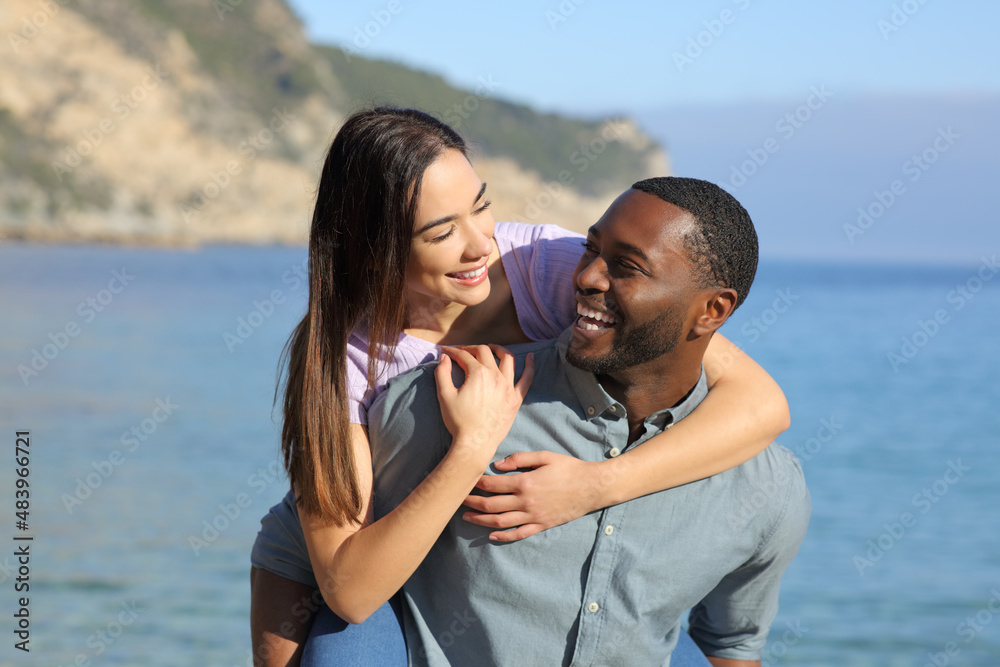 Funny interracial couple on piggyback on the beach