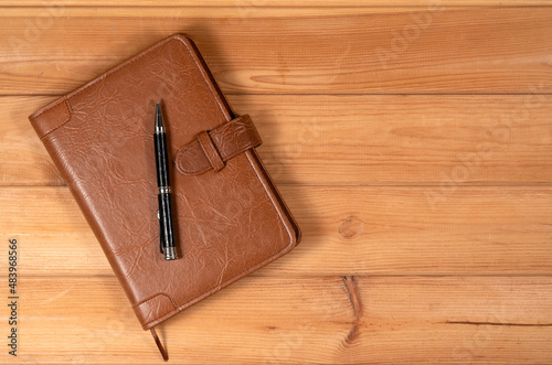 Red color handmade leather notebook cover with notebook and pen inside on wooden background. Stock photo of luxury business accessories.