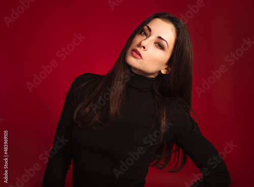 Beautiful confident serious business woman with red lipstick in black sweater posing on dark red background with empty copy space. Closeup