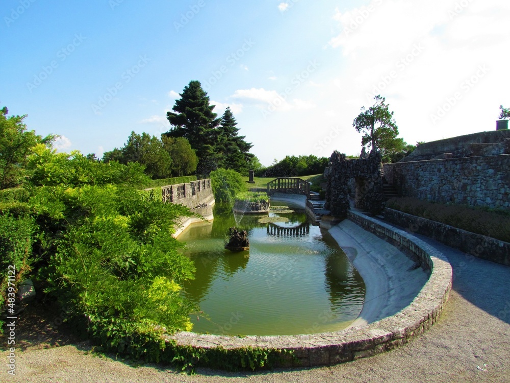 Oval pool at Ferrari garden in Stanjel in Littoral region of Slovenia with a stone bridge and a small island in the middle and a reflection of the bridge in water