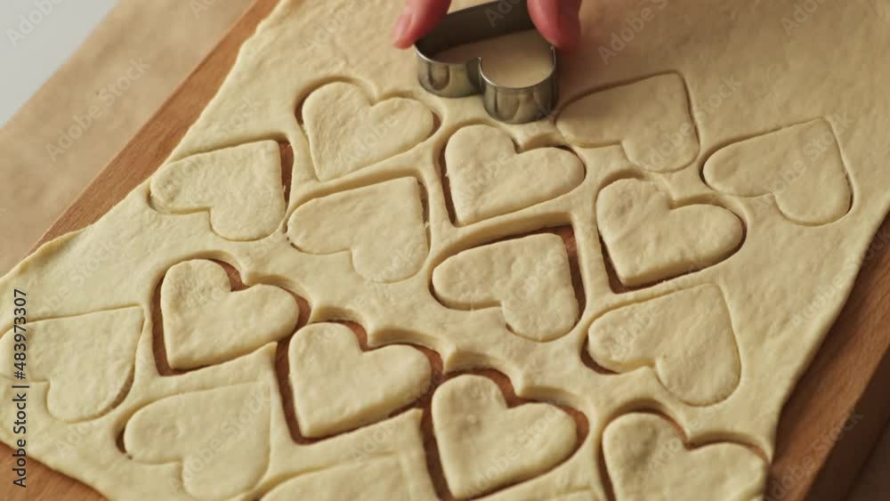 St Valentine's day concept. Homemade bakery. Women's hand cuts puff pastry, making heart shaped cookies on wooden cutting board. St Valentine's day concept. Homemade bakery. Women's hand cuts puff pastry, making heart shaped cookies on wooden cutting board.