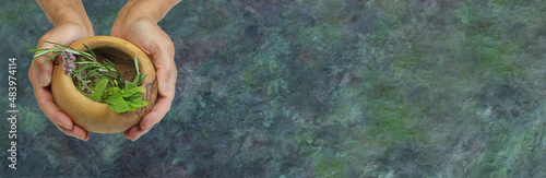 Wicca Message Background Web Banner - female holding olive wood bowl containing selection of common culinary herbs including mint, rosemary, thyme and sage against rustic grunge dark blue green 