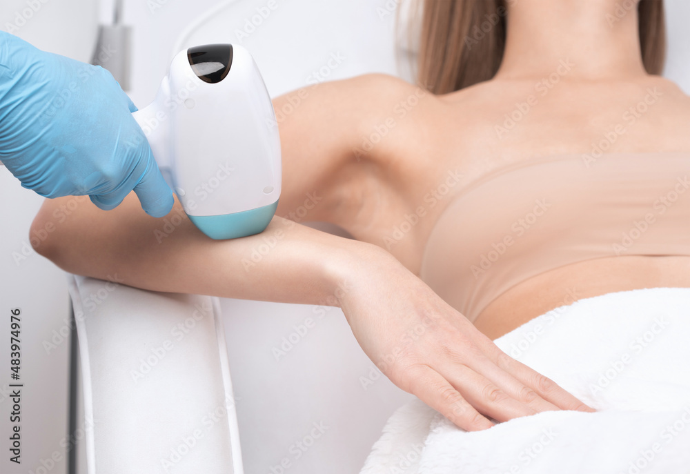 Naklejka premium Elos epilation hair removal procedure on a woman’s body. Beautician doing laser rejuvenation on the lower leg in a beauty salon. Removing unwanted body hair. Hardware ipl cosmetology