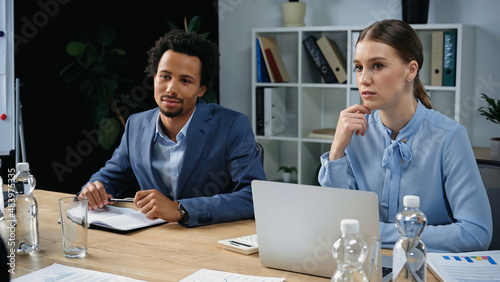 thoughtful interracial business people sitting near laptop and documents in meeting room