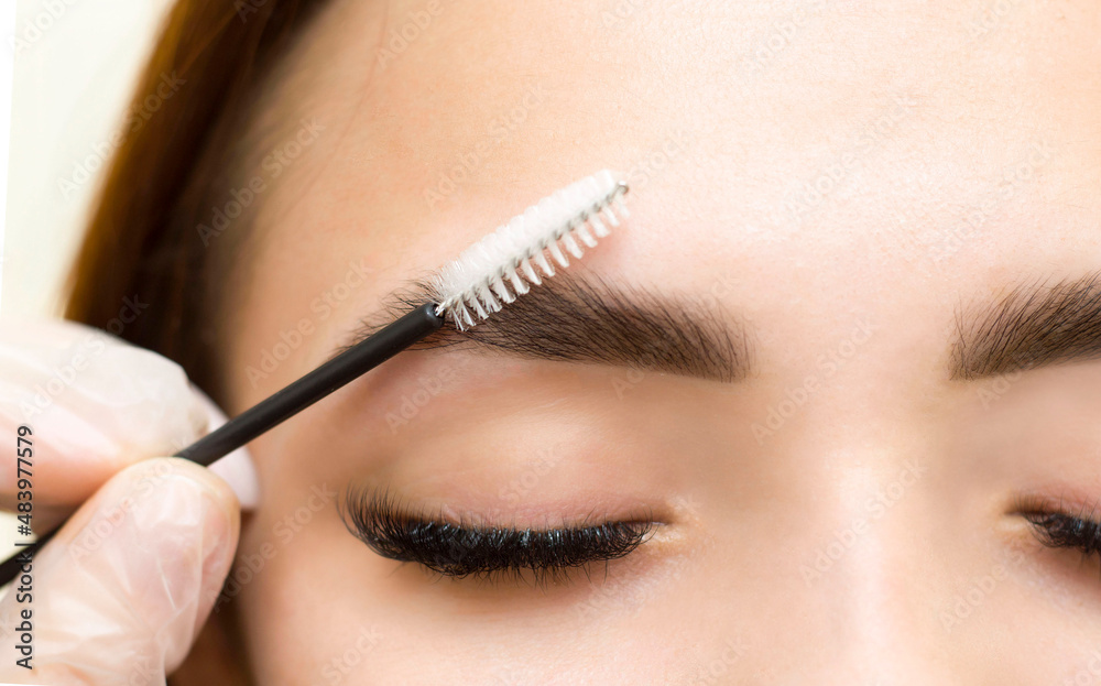 The makeup artist combs his eyebrows with a brush. Eyebrow styling. Permanent makeup. Coloring with henna paint.