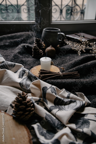 burning candle on a winter table with whool, pine cone and tea cup