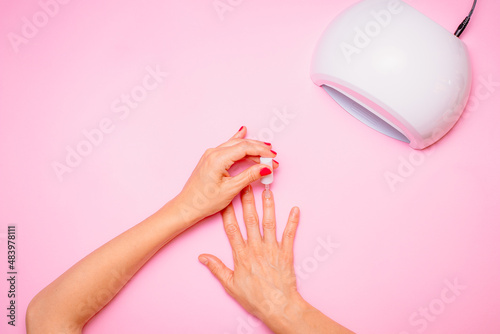 Woman's hand while taking care of her nails on pink background, flat lay