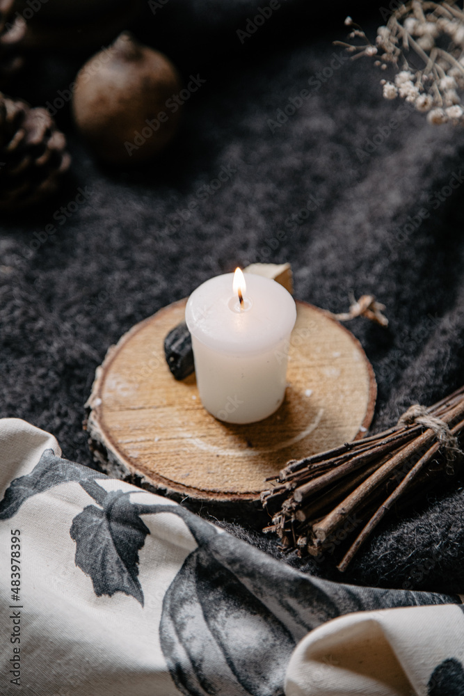 burning candle on a winter table with whool, pine cone and tea cup