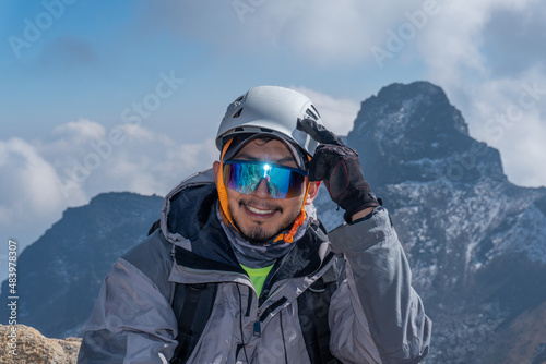 portrait of a climber with helmet and goggles in front of mountains