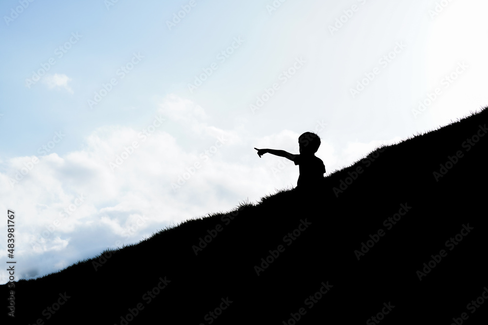 Silhouette of a child on the hill with sky background.