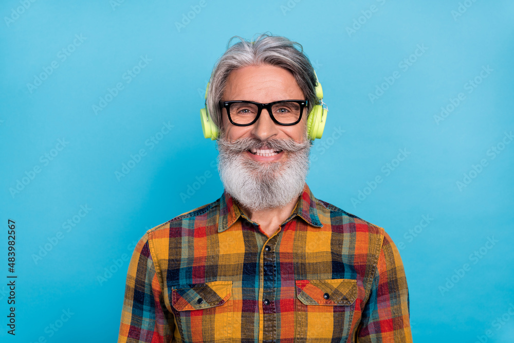 Photo of pretty attractive retired man wear plaid shirt spectacles listening music modern device isolated blue color background Photo of pretty attractive retired man wear plaid shirt spectacles listening music modern device isolated blue color background