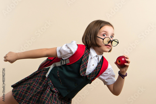 Amazed Open-eyed Little Girl 9s Wearing school uniform and in stylish round glasses with red apple indoor shot. Child hurry up to lunch with healthy snack. photo