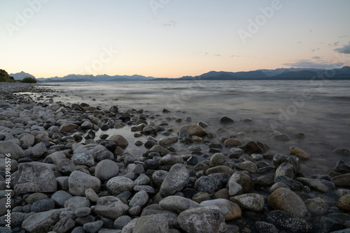 Long exposure shot of Nahuel Huapi lake and the Andes mountains in the background  at sunset. Beautiful blurred water effect  the rocky shore and dusk colors in the landscape. 