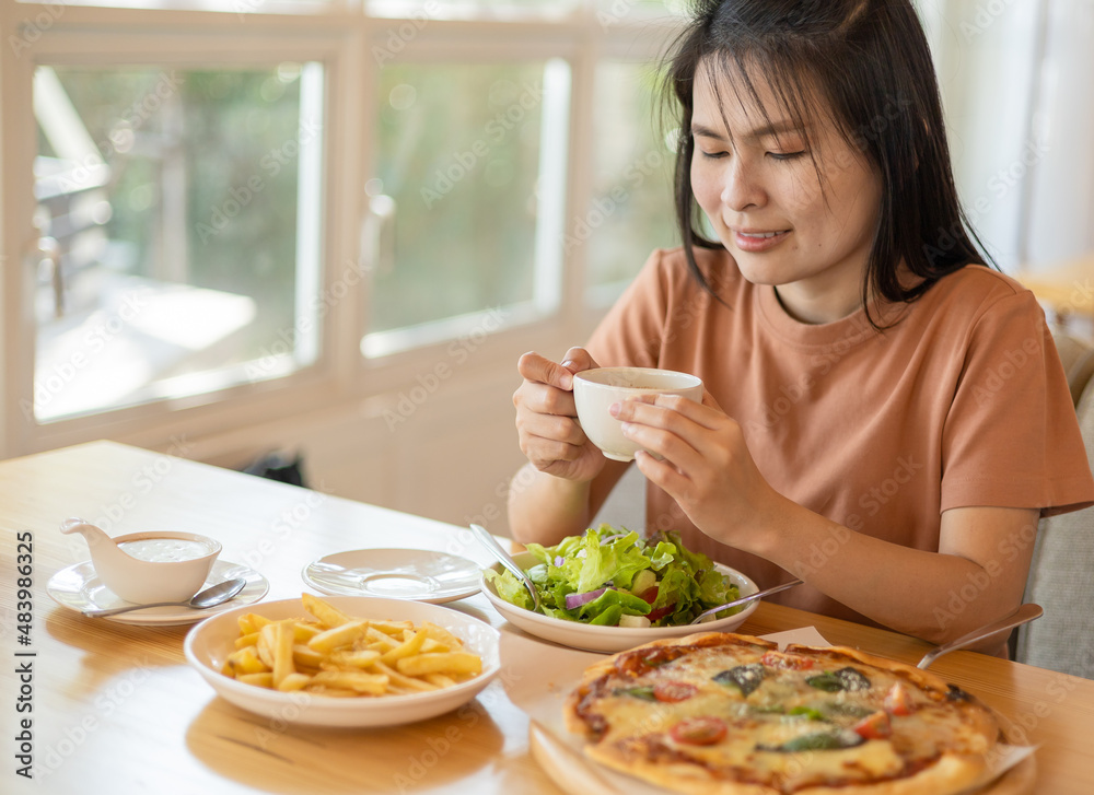 A woman drinking coffee with feeling happy and enjoy to eat food in the restaurant in leisure time. dine in the restaurant, eating delicious served hot pizza and salad. Eating concept. Italian food.
