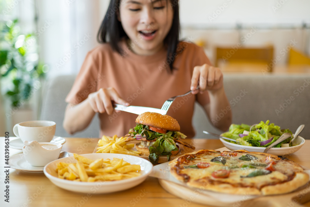 Young Asian woman smiling with her food, pizza, hamburger, A woman holding fork and steak knife feeling happy and enjoy to eat food in the restaurant. Enjoy eating concept. Italian food.