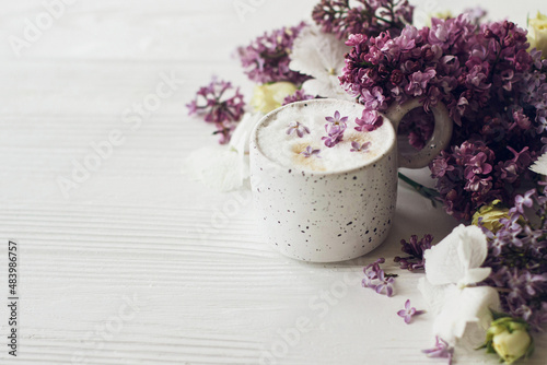 Delicious coffee with lilac petals, rose and lilac branch on rustic white wooden background. Hello spring. Space for text. Happy mothers day. Good morning still life