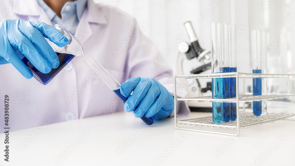 Fototapeta premium Scientist pouring a beaker with clear solution into a test tube in pharmaceutical research laboratory. Innovation Concept.