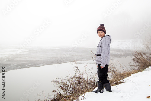 a boy stands on the bank of a river on a spring day before the ice breaks