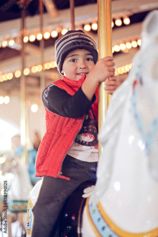 Young boy wearing a red vest on a horse at a carrousel.