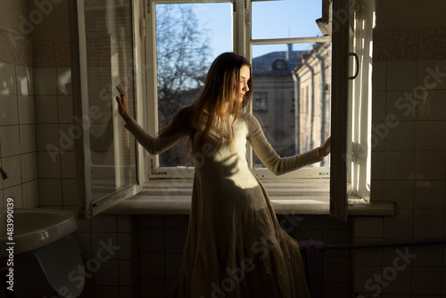 woman in dress stands near the window