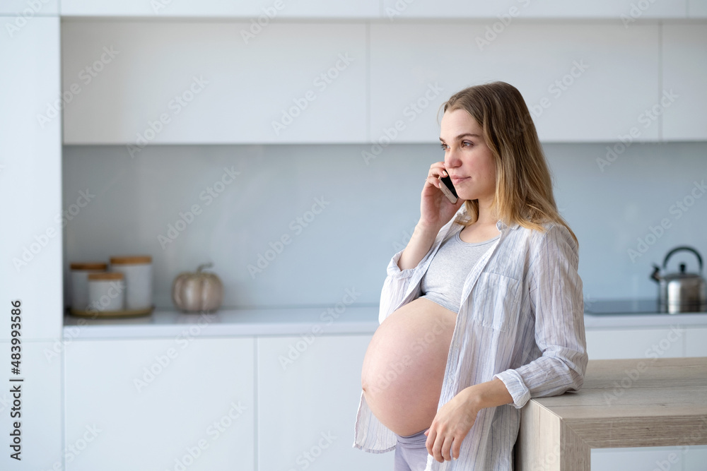 Happy pregnant woman is sitting at home in the kitchen with a mobile phone in her hands. Happy pregnant woman is sitting at home in the kitchen with a mobile phone in her hands.