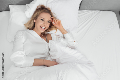 adorable young lady laying in soft and comfortable bed with snowy pillows and blanket. Smile happy and look at something