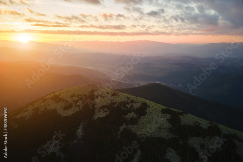 Aerial view of amazing scenery with foggy dark mountain peak covered with forest pine trees at autumn sunrise. Beautiful wild woodland with shining rays of light at dawn