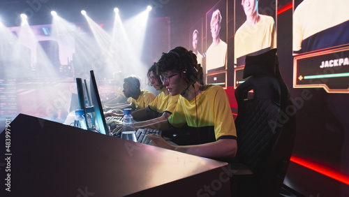 Anxious teen gamer esportsman in glasses and headphones starting to play shooter on computer while sitting near team during professional gaming competition battle