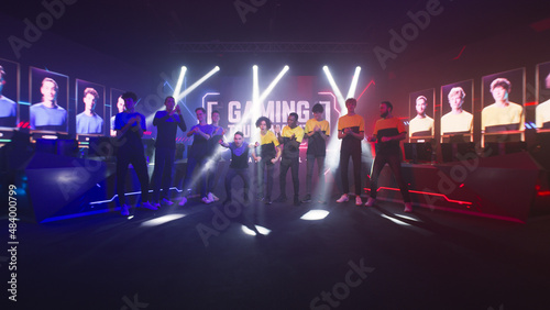 Canvas Print Group of teammates esport gamers walking and clapping hands then standing in front of monitor with gaming tournament banner at start of championship