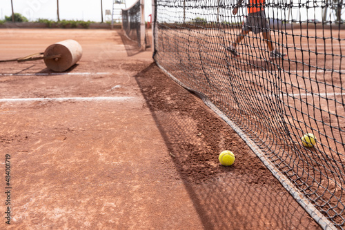 Tennis balls near net with heavy roll and maintenance person on clay court on sunny day outdoors. Sports training concept © Josu Ozkaritz