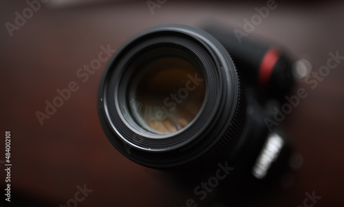 Photography as hobby. Close up view of the lens of a D-SLR camera against dark wood background.