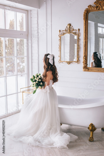 Beautiful bride with bouquet in wedding dress sitting in studio. Bride view from the back photo