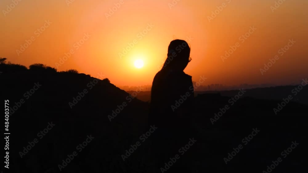 Sunset silhouette of one woman walking at the time of sunset. Female enjoying evening at hill. Weekend fun Sunset silhouette of one woman walking at the time of sunset. Female enjoying evening at hill. Weekend fun